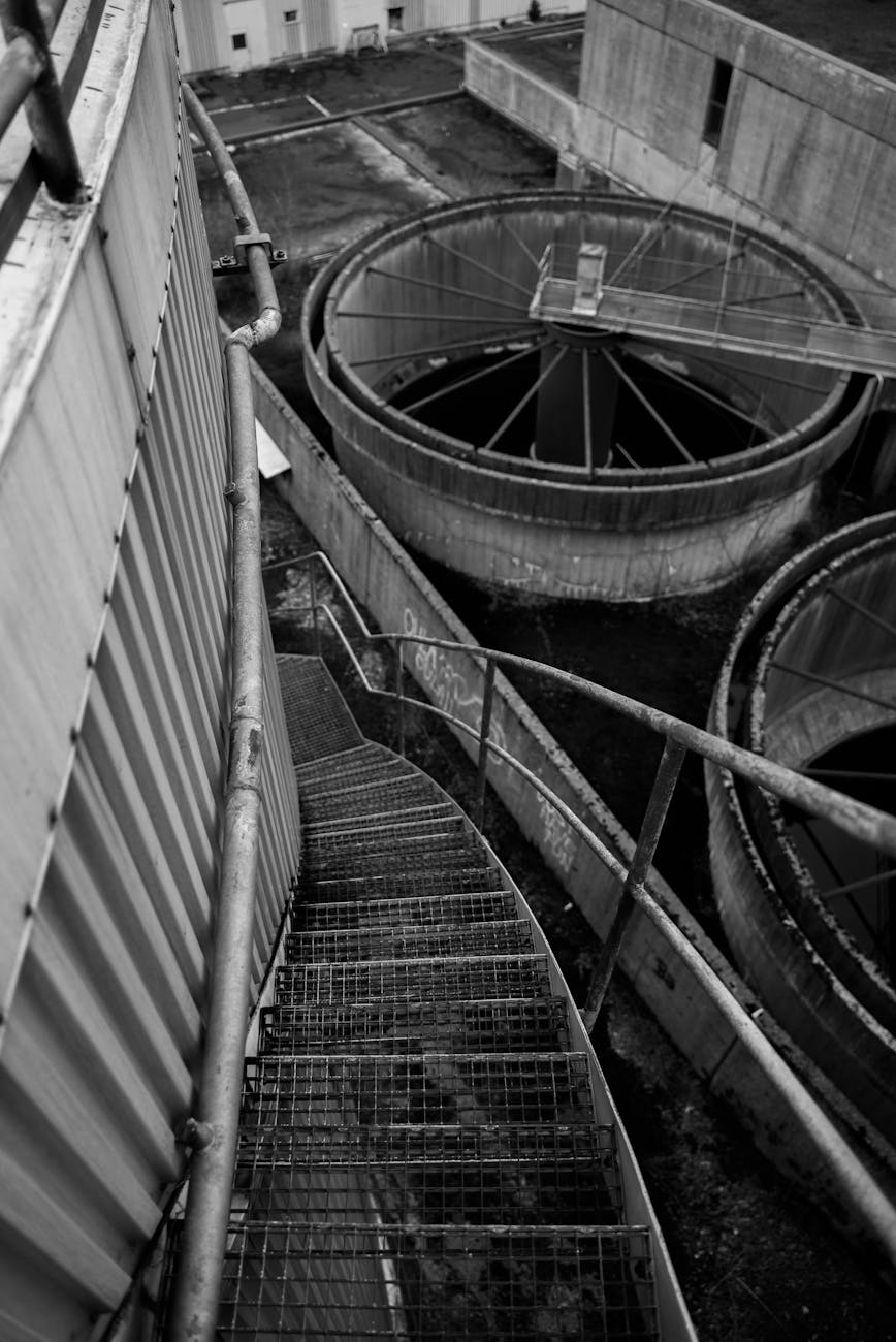 Black and white image of an industrial metal staircase descending into a factory setting.