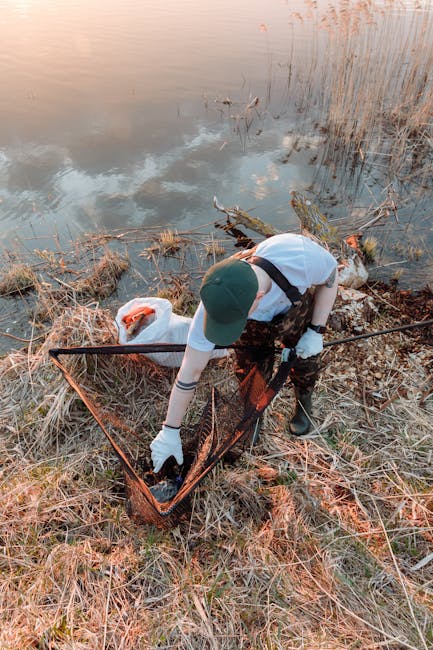 A dedicated volunteer uses a net to clean trash by a serene riverside during sunset.
