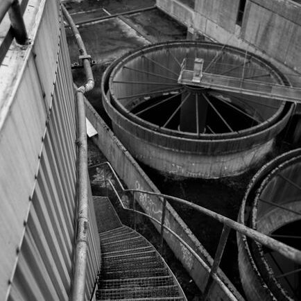 Black and white image of an industrial metal staircase descending into a factory setting.