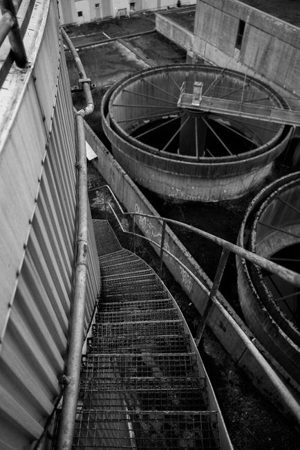 Black and white image of an industrial metal staircase descending into a factory setting.